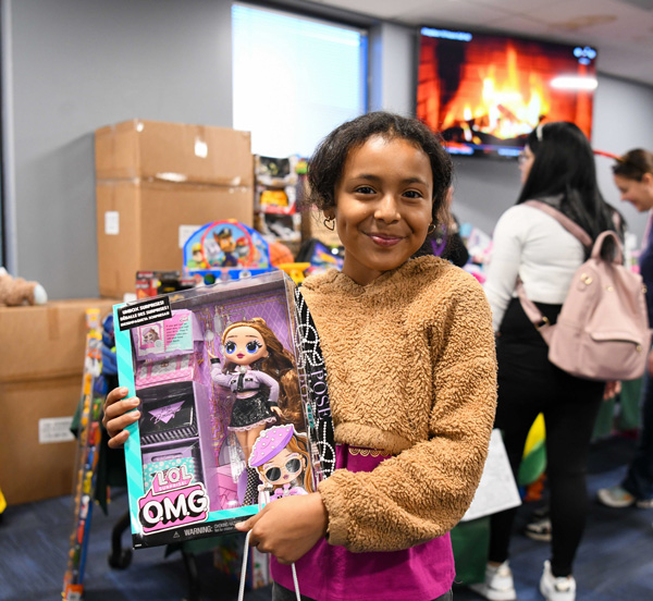 A child smiling while holding her new doll at a holiday book and toy distribution.