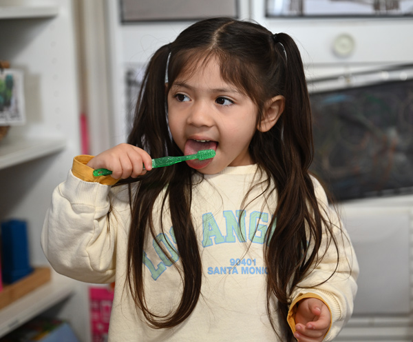 A child brushing her teeth with a green toothbrush.