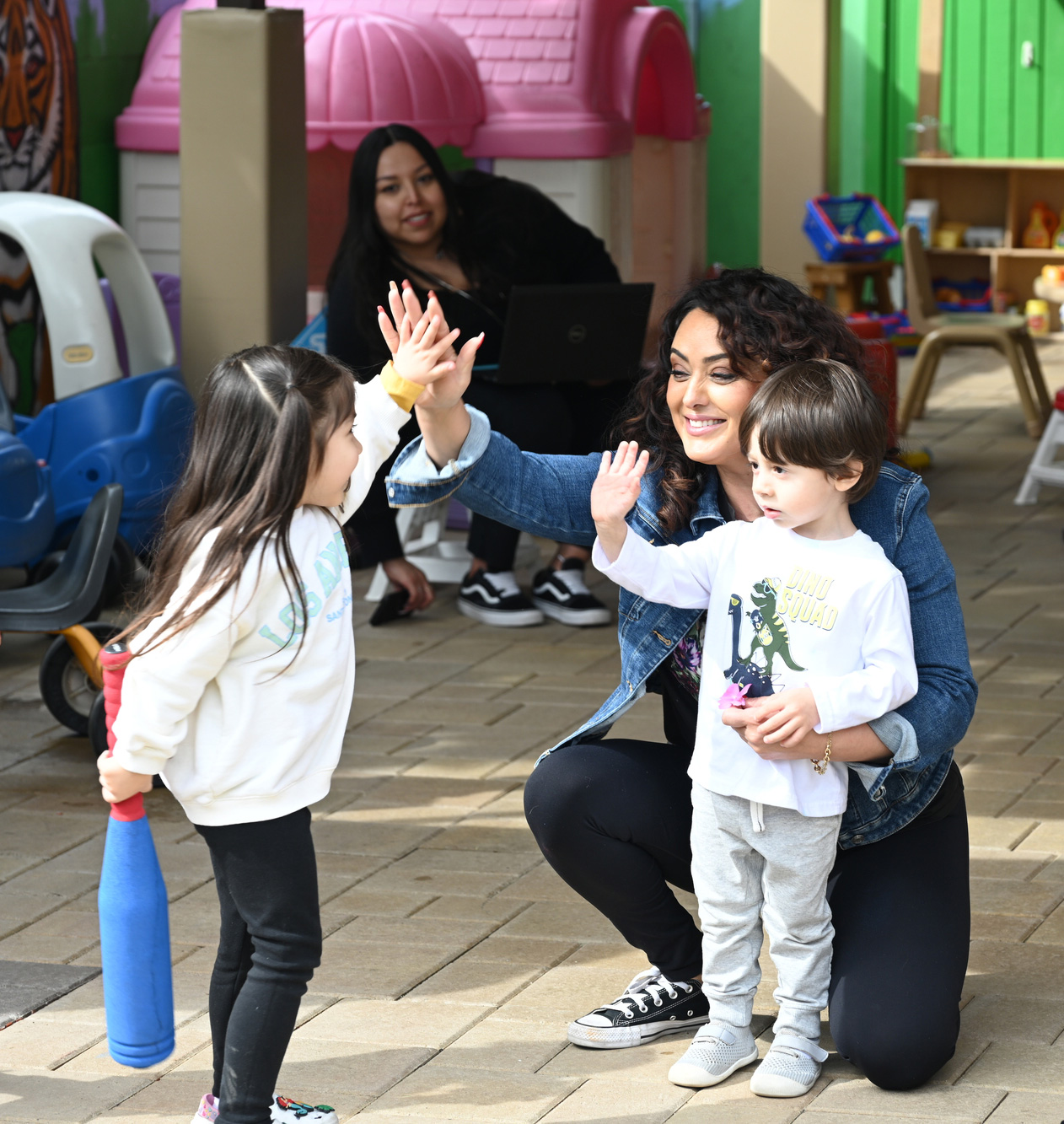 A child care provider smiling while giving children high fives.