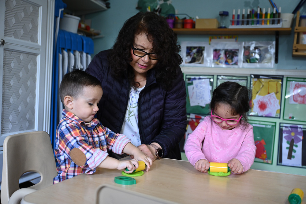 A child care provider playing with play dough on the table.