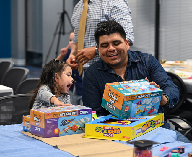 A father and child smiling while looking at new toys together.