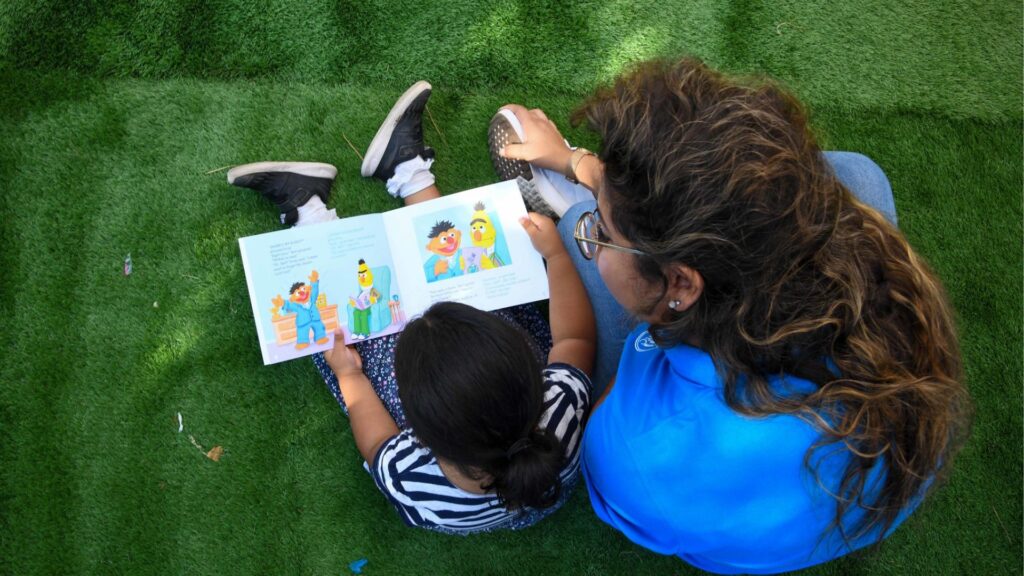 A young girl is reading a book with a young preschool teacher.